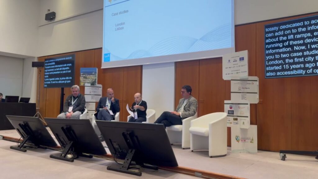 William Del Negro, CEO di Willeasy, interviene al talk “IT and Technologies” durante il World Summit on Accessible Tourism a Torino. Seduto al centro del panel insieme ad altri relatori, parla di open data e tecnologie digitali per l’accessibilità. Sullo sfondo è proiettata una slide con i case studies di Londra e Lisbona.