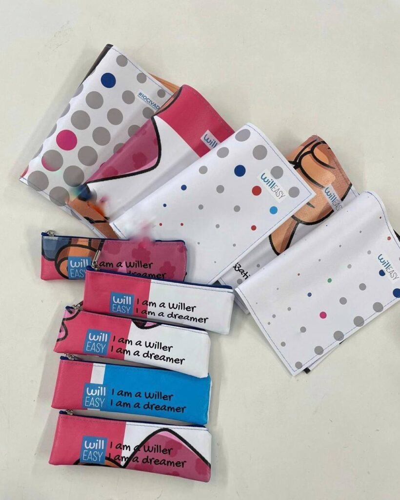 Gadget realizzati con materiali riciclati: astucci e pochette Willeasy prodotti recuperando gli striscioni dell&rsquo;evento Accessibility for Future, con grafiche colorate e dettagli personalizzati, disposti su una superficie chiara.