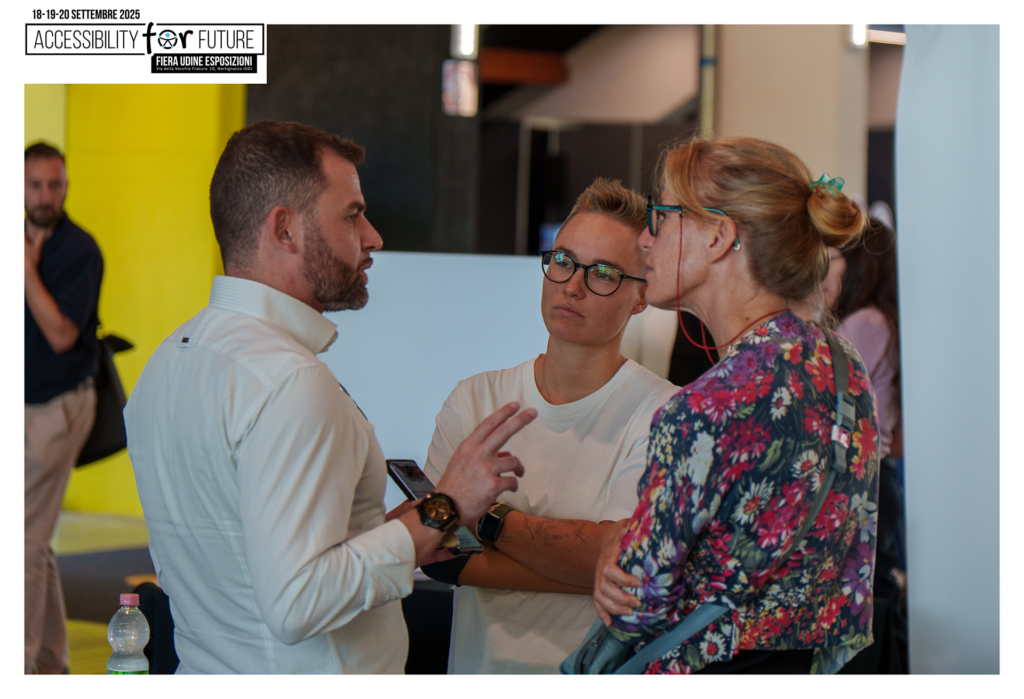 Fotografia scattata durante l'evento "Accessibility For Future" (settembre 2025) presso la Fiera Udine Esposizioni. L'immagine ritrae una parte del team di In&Valid impegnata in una conversazione informale con altri partecipanti all'interno del padiglione fieristico.