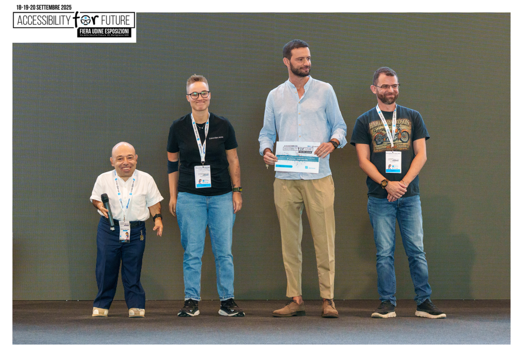 Fotografia scattata sul palco dell'evento "Accessibility For Future" presso la Fiera Udine Esposizioni. All'estrema sinistra c'è William Del Negro, CEO di Willeasy. Alla sua destra sono presenti tre membri del team di In&Valid.