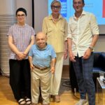 Ritratto di gruppo durante la presentazione di InclusivAPP. Da sinistra: Silvia Moras (Palazzo del Fumetto), William Del Negro (Willeasy), una relatrice ospite e Antonio Testa (AT Media). William Del Negro indossa una polo azzurra con il logo "will EASY". Sullo sfondo, uno schermo proietta una slide con il logo dell'app e la scritta "Palazzo del Fumetto - Lingua e Istruzioni".