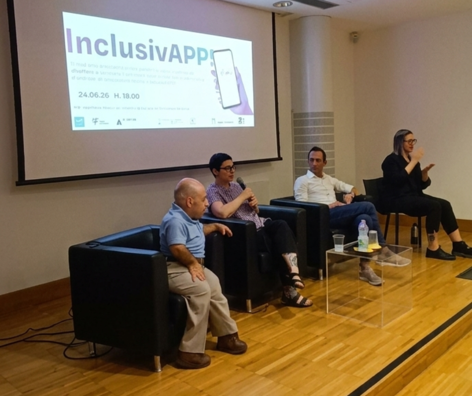 Quattro persone sul palco di un auditorium durante la presentazione del progetto InclusivAPP. Da sinistra a destra: William Del Negro di Willeasy, Silvia Moras del Palazzo del Fumetto (mentre parla al microfono), Antonio Testa di AT Media e Nadia Pers, interprete LIS che traduce la presentazione nella lingua dei segni. Sullo sfondo è proiettata la slide dell'evento.